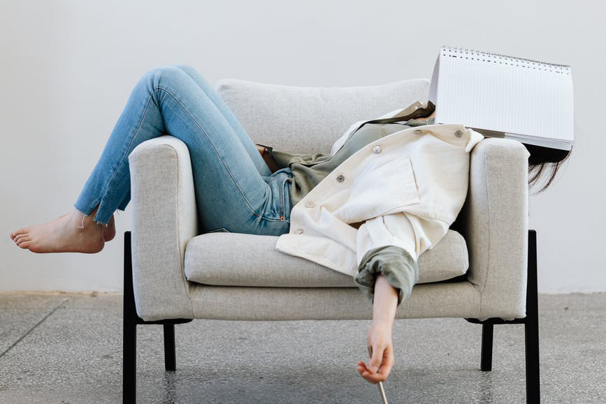 woman lying on a sofa with a notebook on her face
